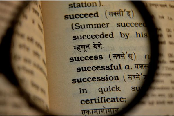 A magnifying glass highlights the word "success" and its translations in a dictionary.
